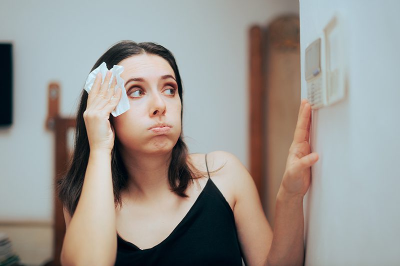 woman having heating or cooling problem looking at thermostat